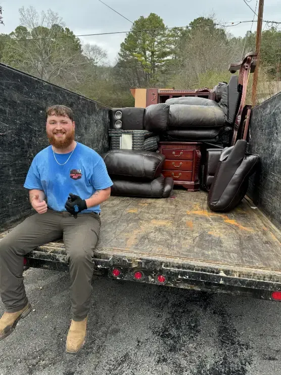 A man is sitting on the back of a dumpster filled with furniture.