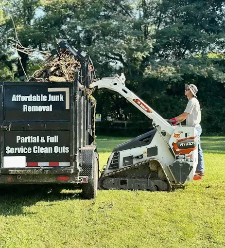 A man is using a bulldozer to remove junk from a dumpster.