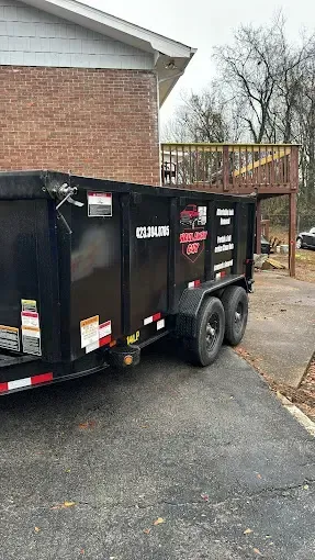 A dumpster trailer is parked in front of a brick house.