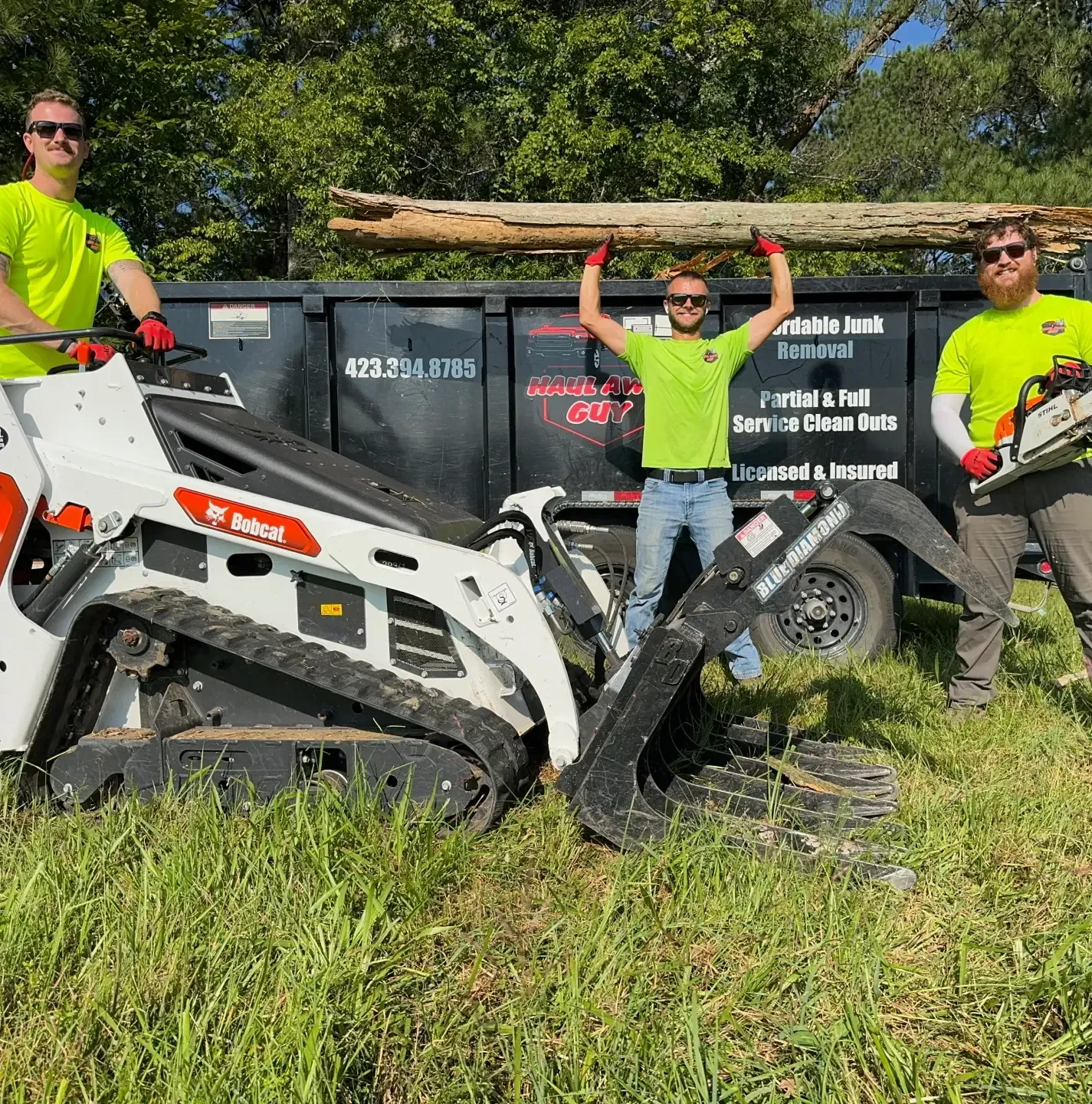 Three men are standing next to a bobcat tractor and a dumpster.