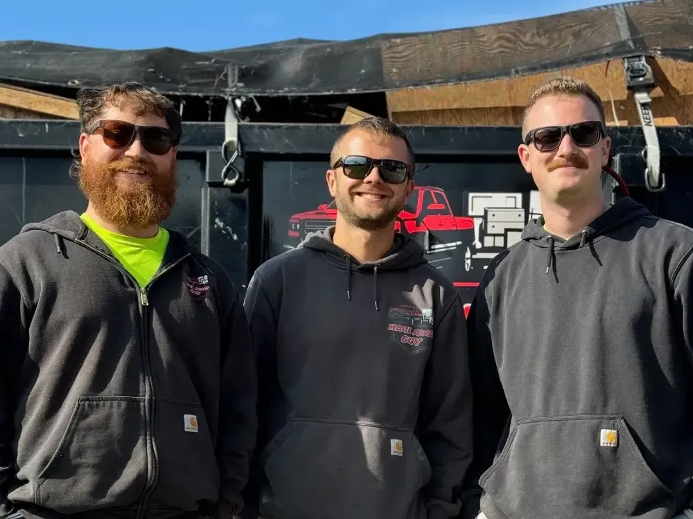 Two men are standing in front of a trailer that says haul away guy