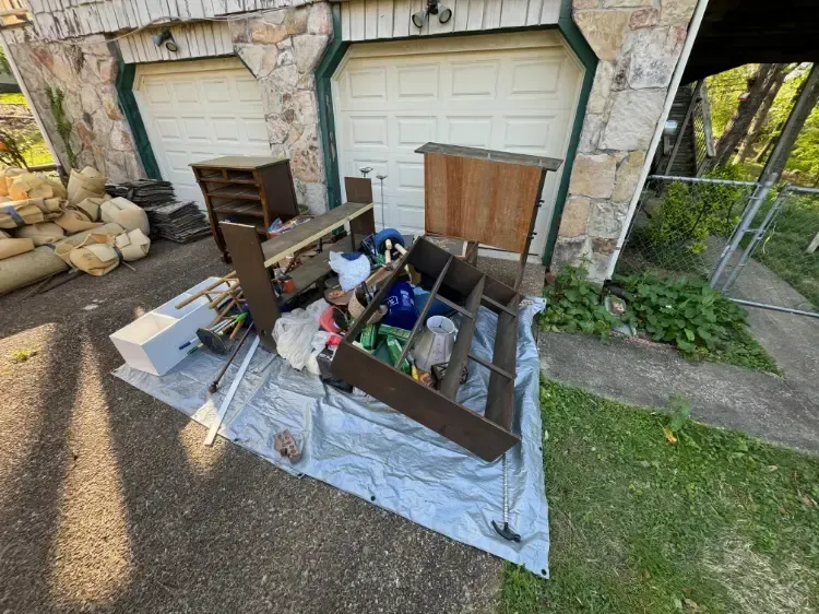 A pile of furniture is sitting on a tarp in front of a garage door.