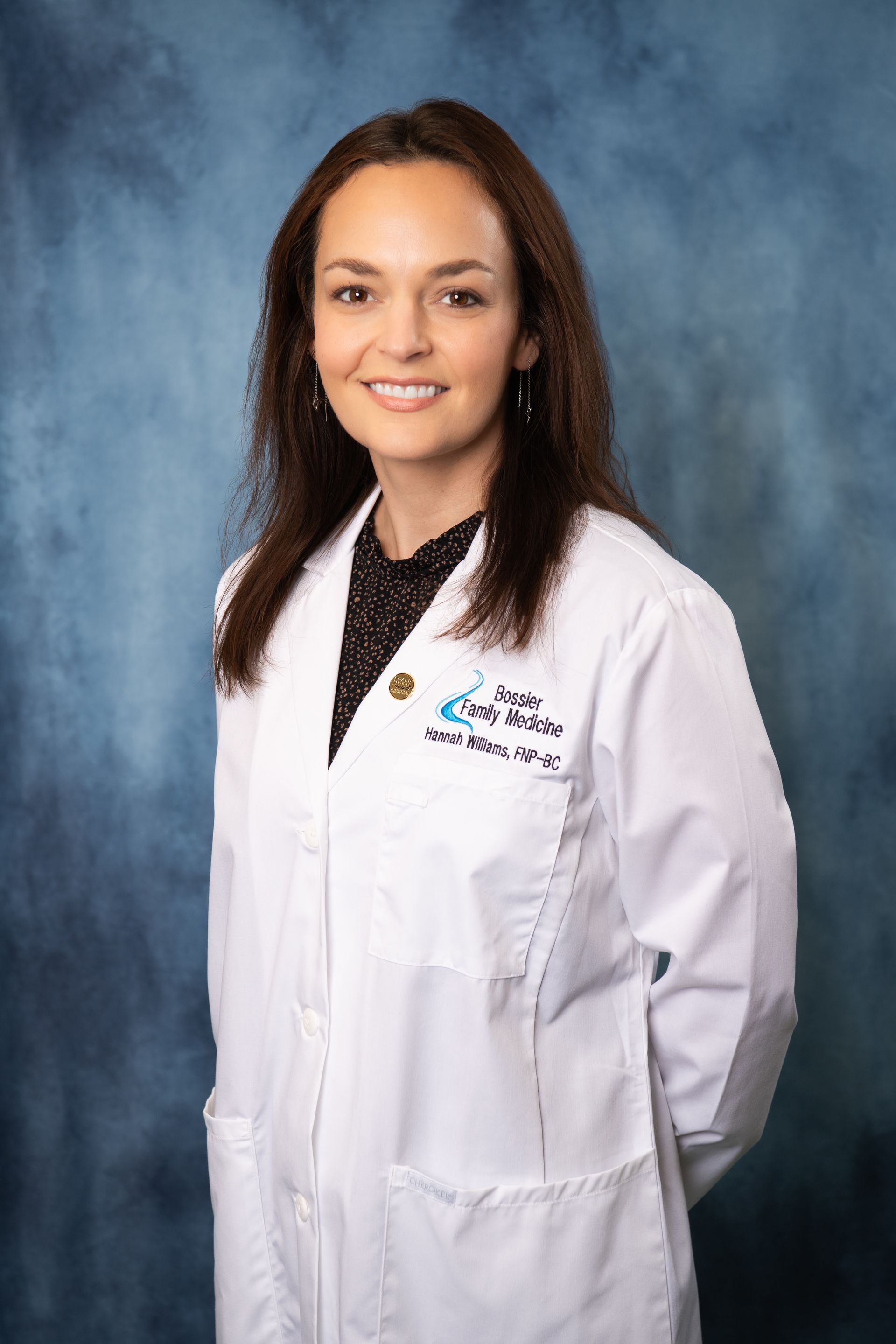 A woman in a white lab coat is standing in front of a blue background.