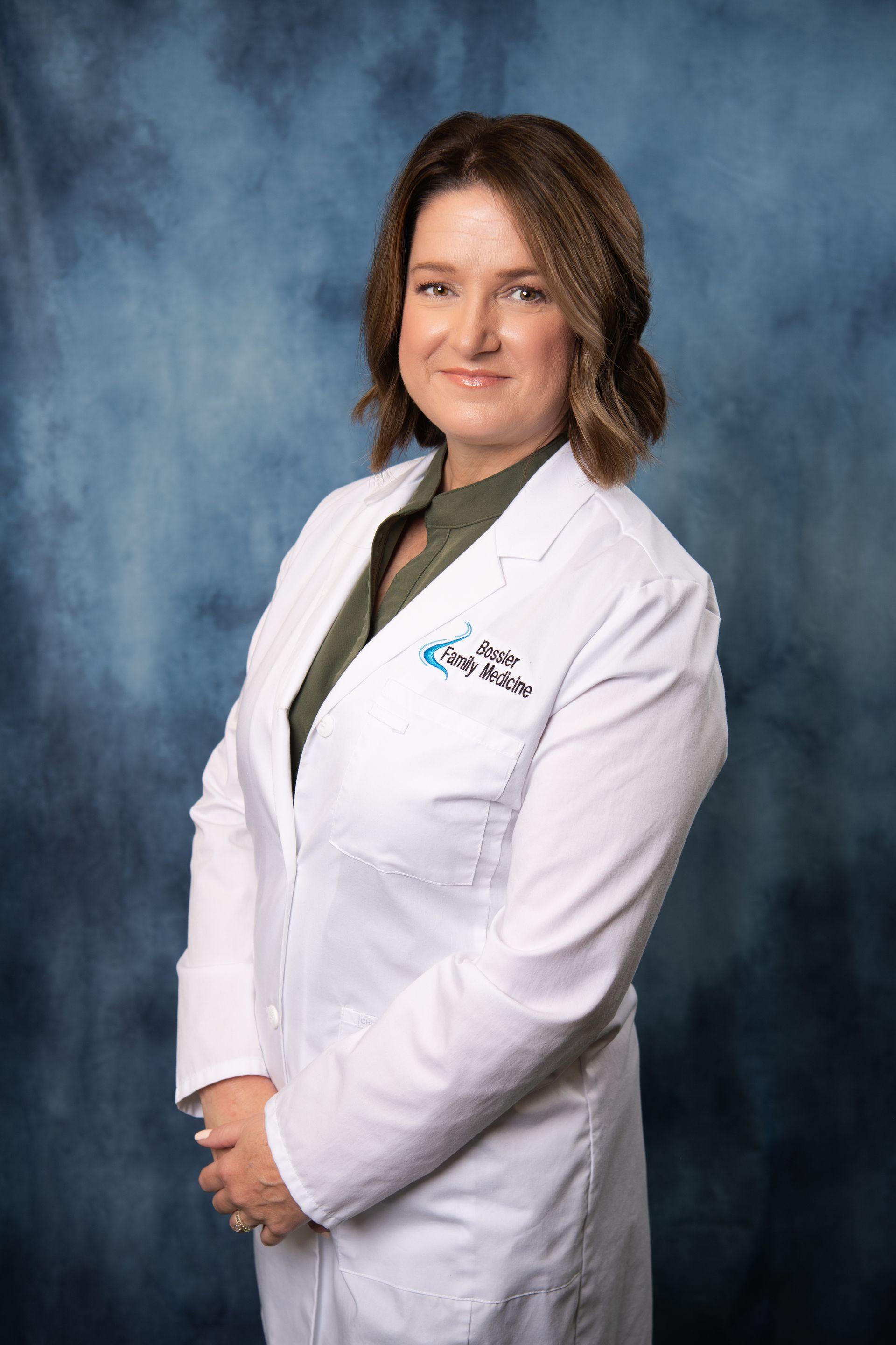 A woman in a white lab coat is standing in front of a blue background.