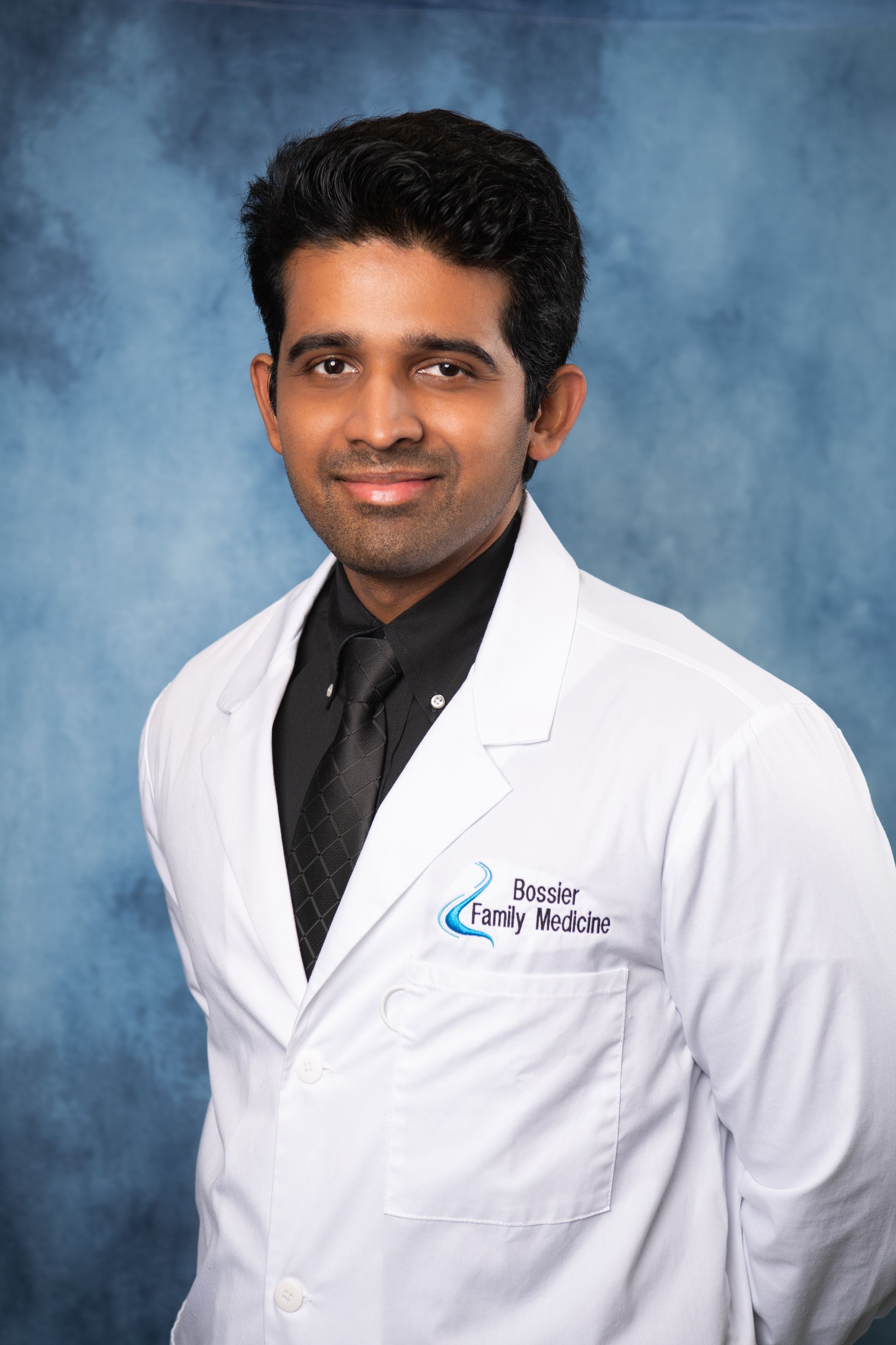 A man wearing a white lab coat and a purple tie