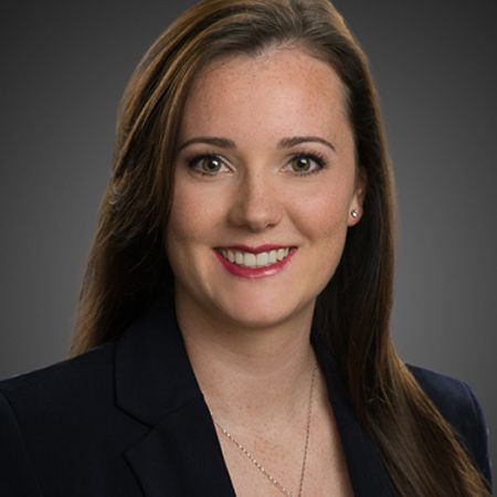 A woman in a suit and necklace is smiling for the camera.