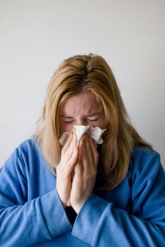 A woman in a blue sweater is blowing her nose into a napkin.