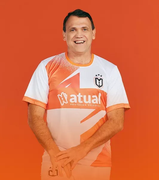 Homem sorrindo com uma camisa esportiva laranja e branca contra um fundo laranja.