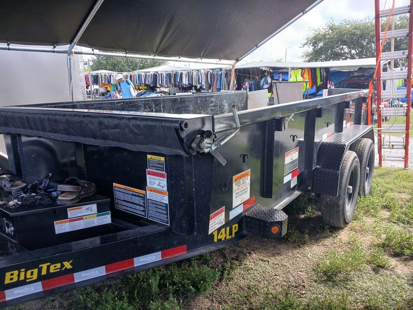 Black 14LP Big Tex trailer under a canopy, parked outdoors on grass.