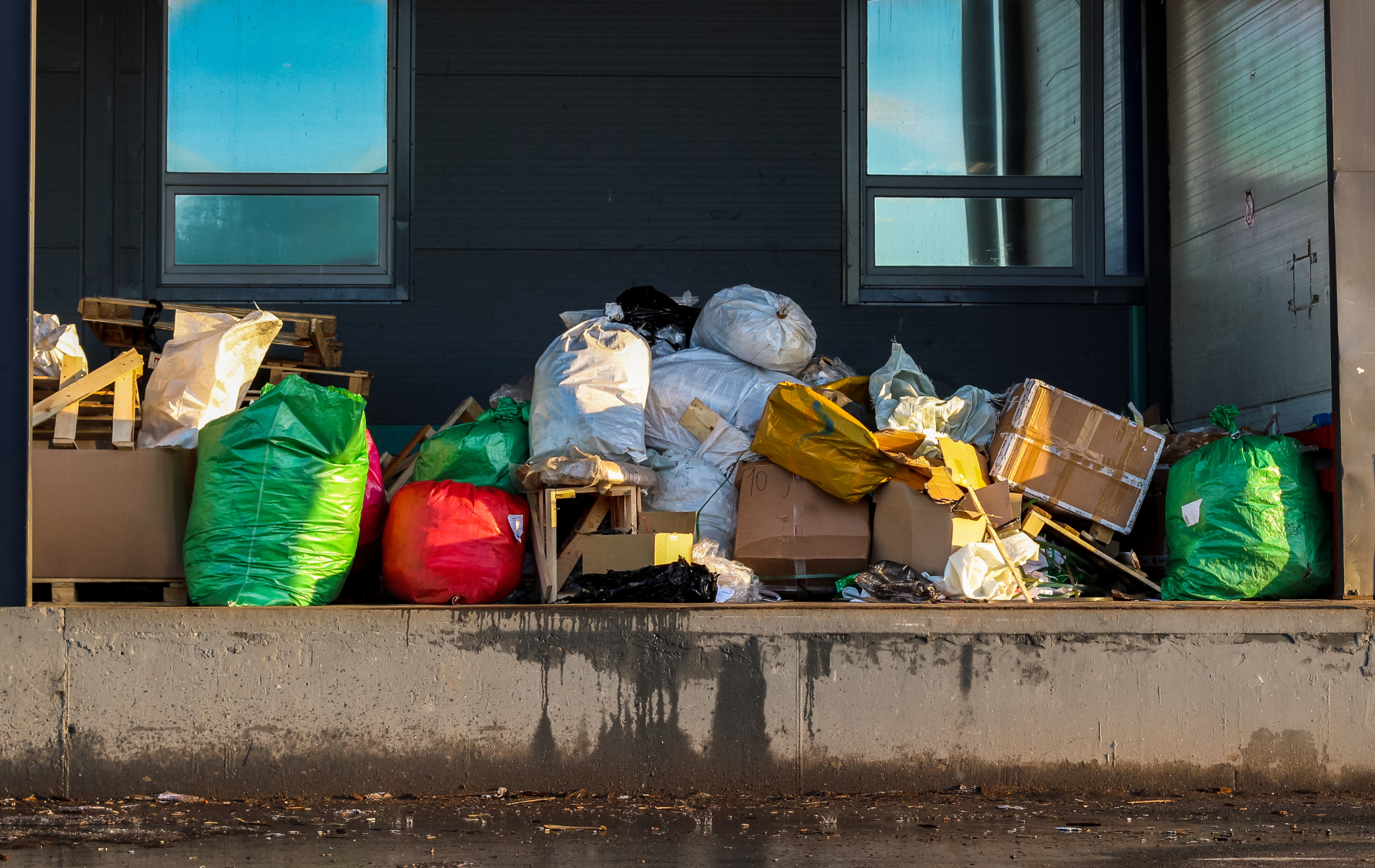 Pile of trash bags, cardboard boxes, and waste overflowing a loading dock.