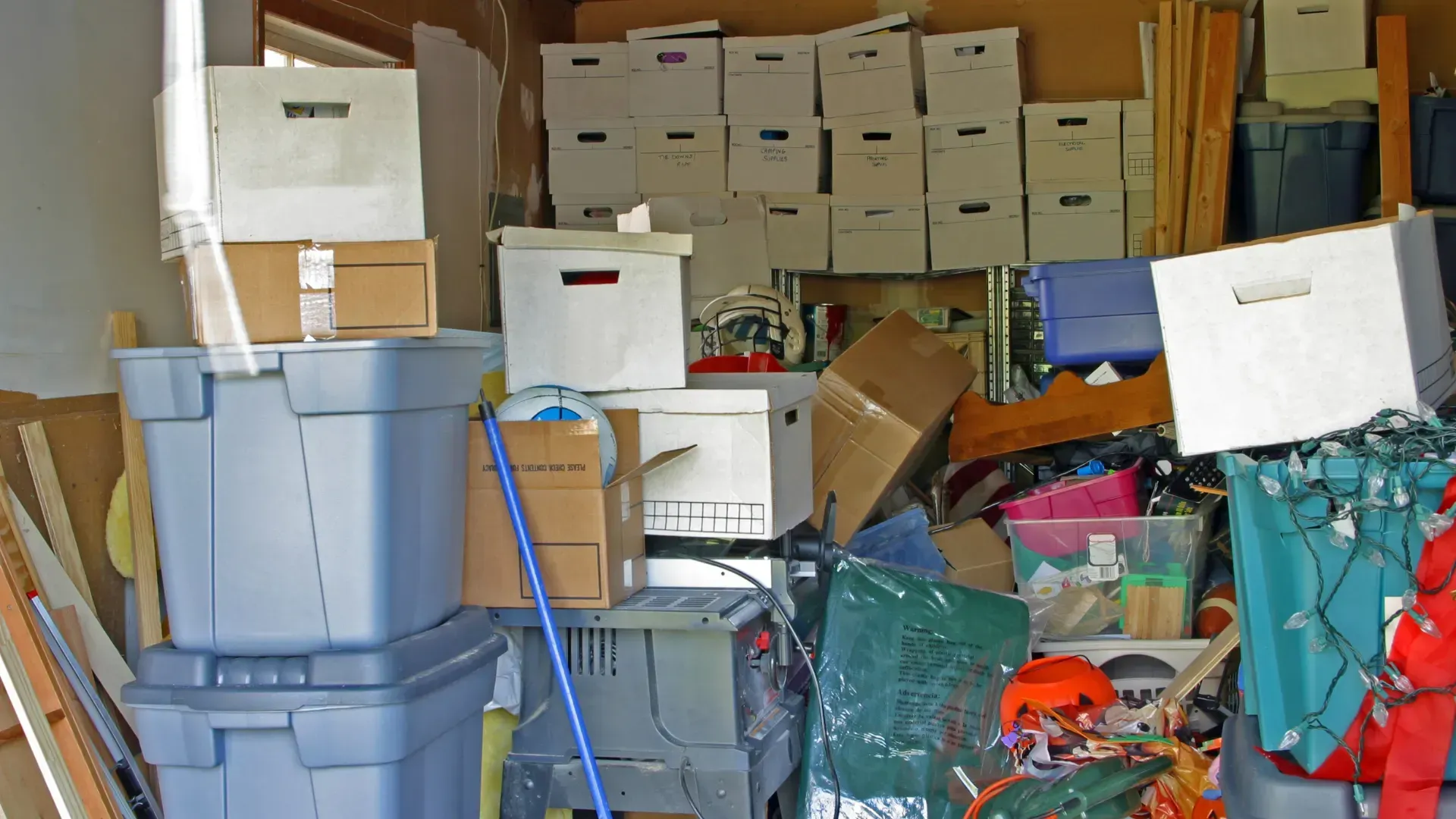 Cluttered garage with stacked storage bins, boxes, and various items. Overstuffed space.