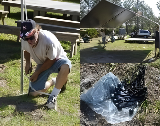 Man kneeling, securing a pole on grass. A large tarp is overhead. Bundle of black cords on ground.