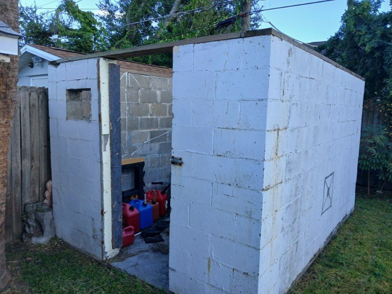 Concrete block shed with open door, fuel cans visible, set on grass.