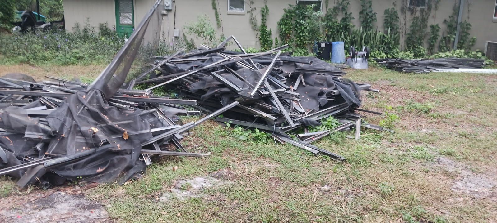 Pile of black debris with metal frame on grassy lawn; building in the background.