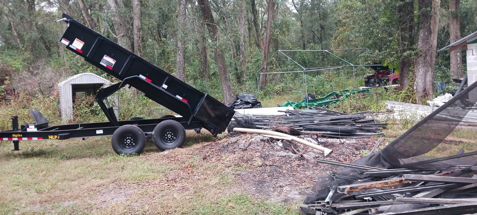 A black dump trailer unloading debris onto a pile of dirt and trash, outdoors.