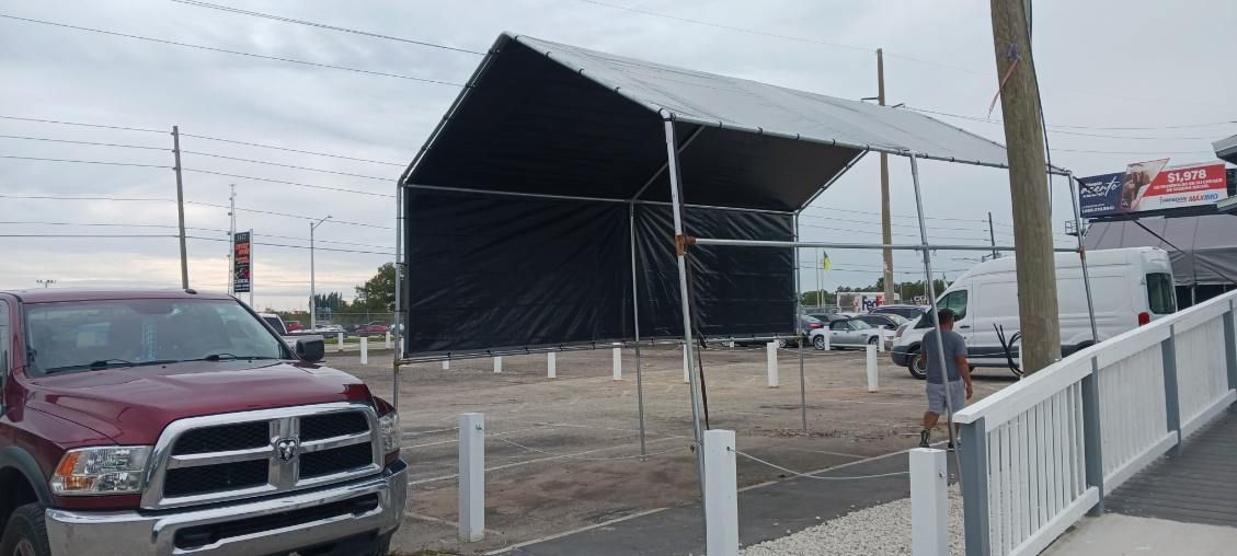 A red pickup truck is parked in front of a black tent set up in a dirt lot.