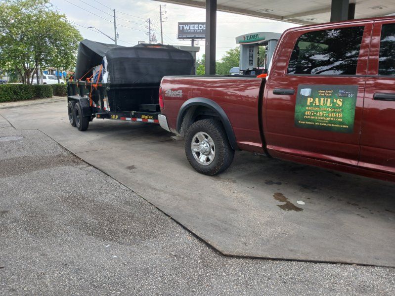 Red truck towing a trailer with a black container at a gas station.