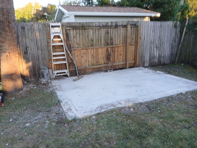 A weathered wooden fence with a concrete pad and a ladder leaning against it.