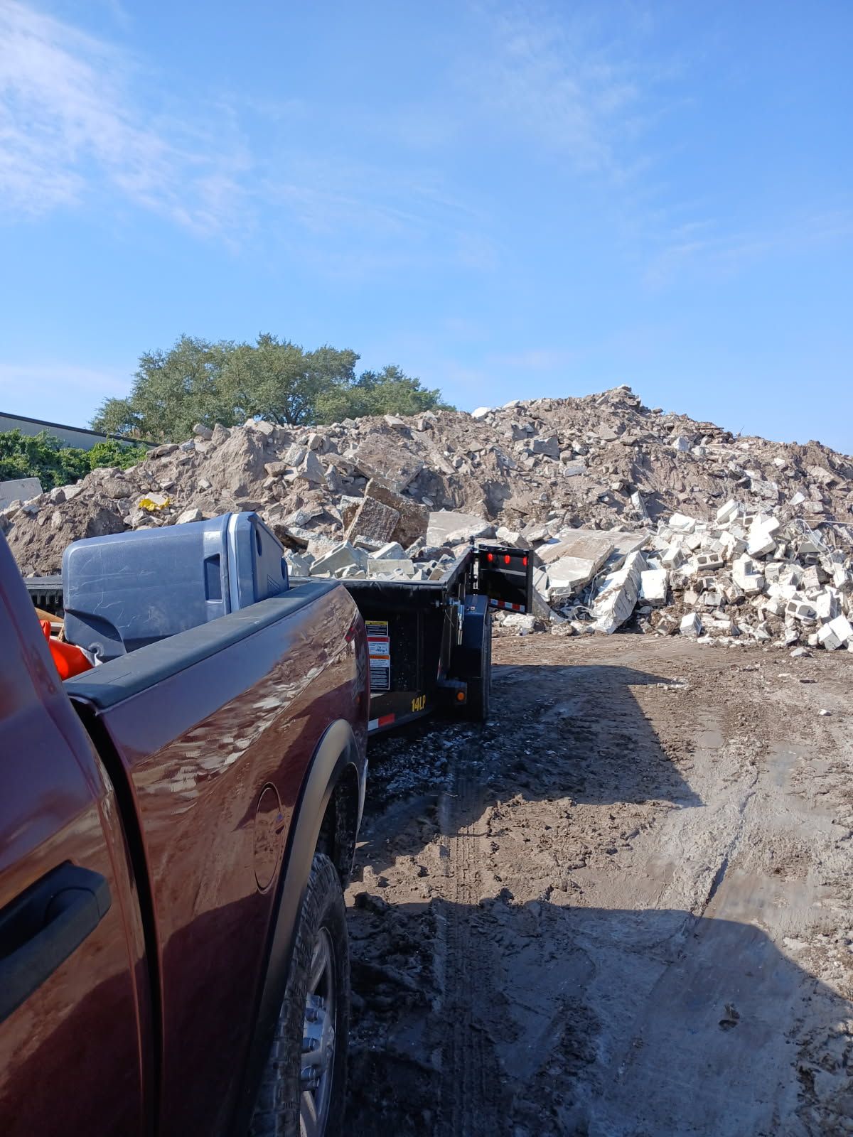 A red pickup truck with a trailer, beside a large pile of rubble under a blue sky.