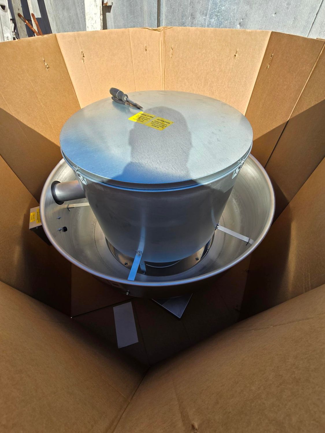 A metal bowl with a lid is in a cardboard box
