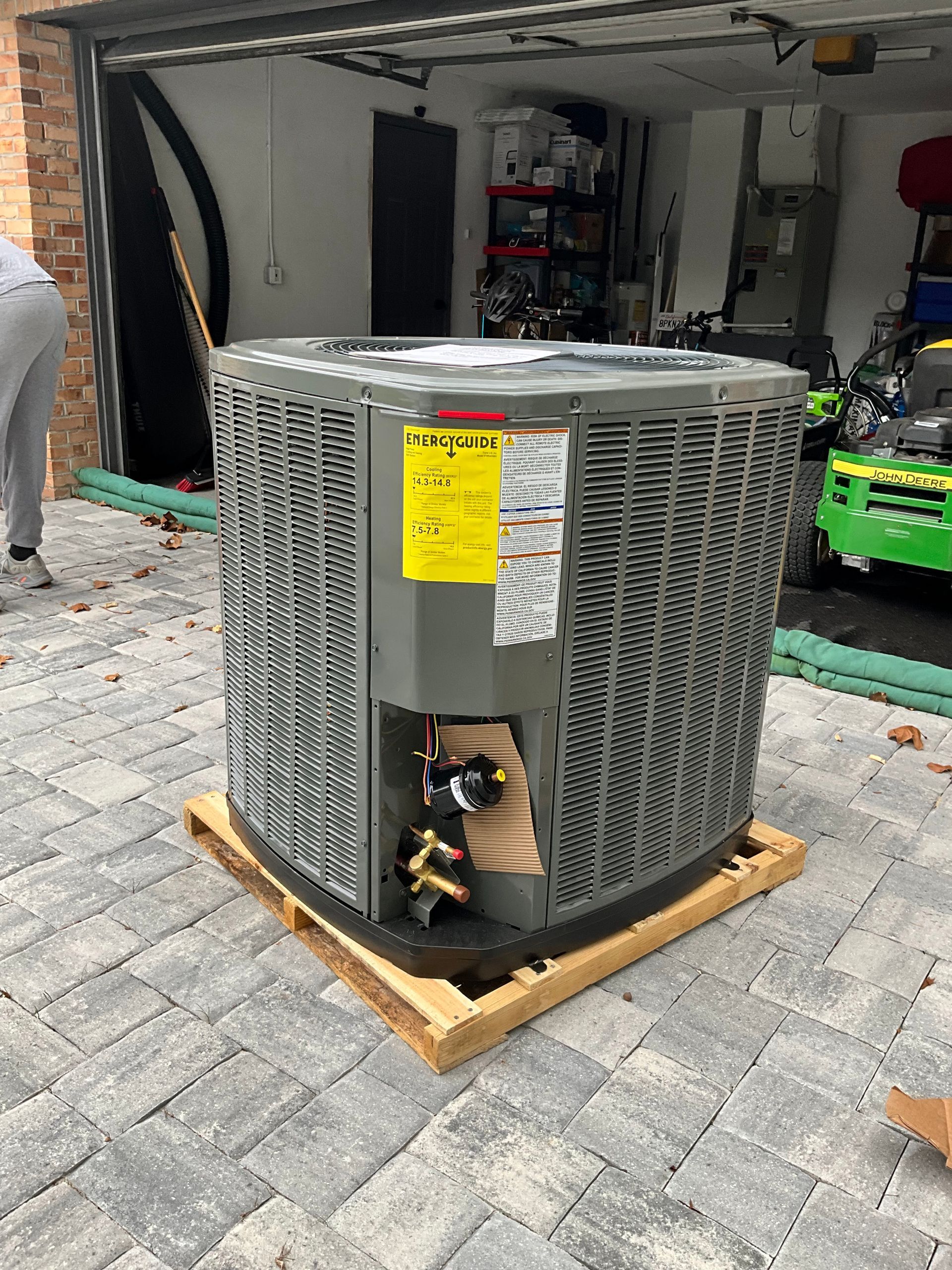 An air conditioner is sitting on a wooden pallet in front of a garage.