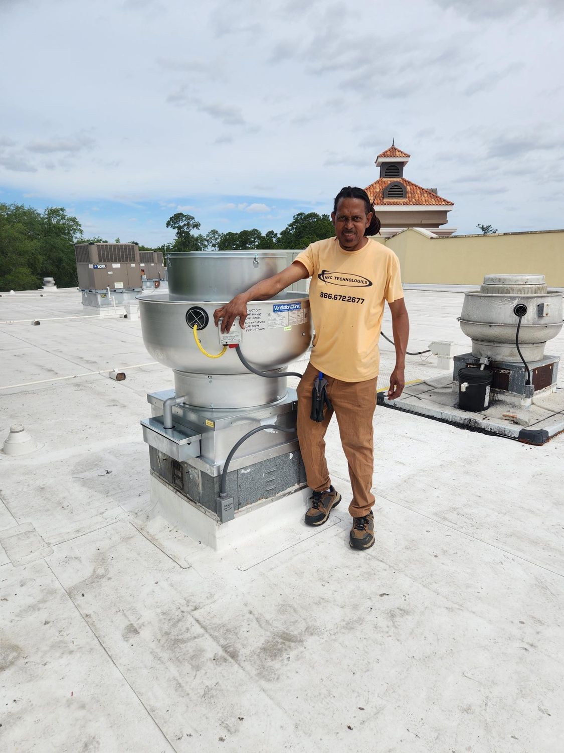 A man is standing on a roof next to a fan.