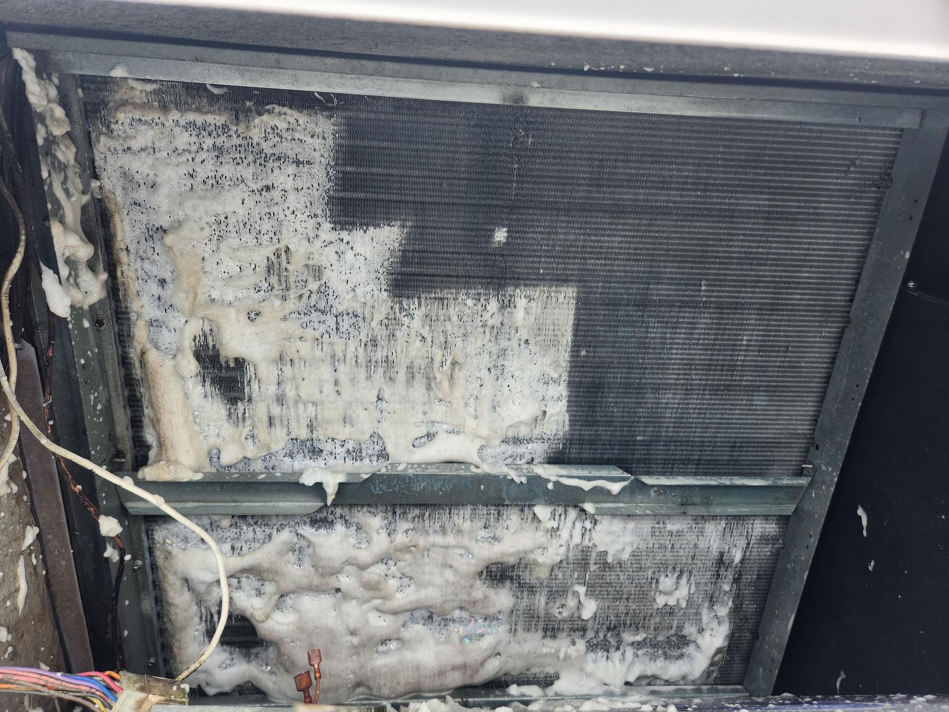 A close up of a dirty air conditioner with foam coming out of it.