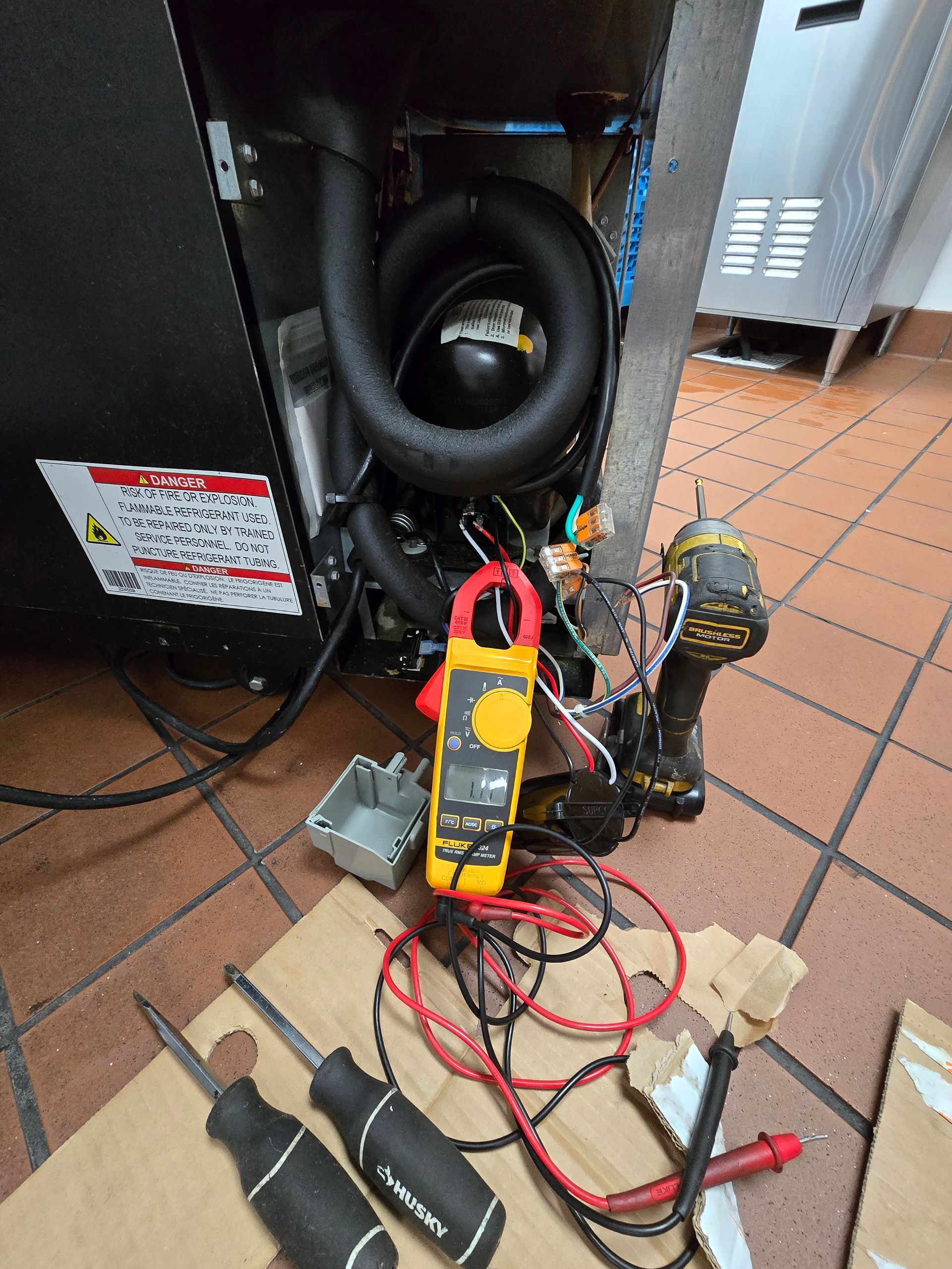 A refrigerator is being repaired with tools and a clamp.