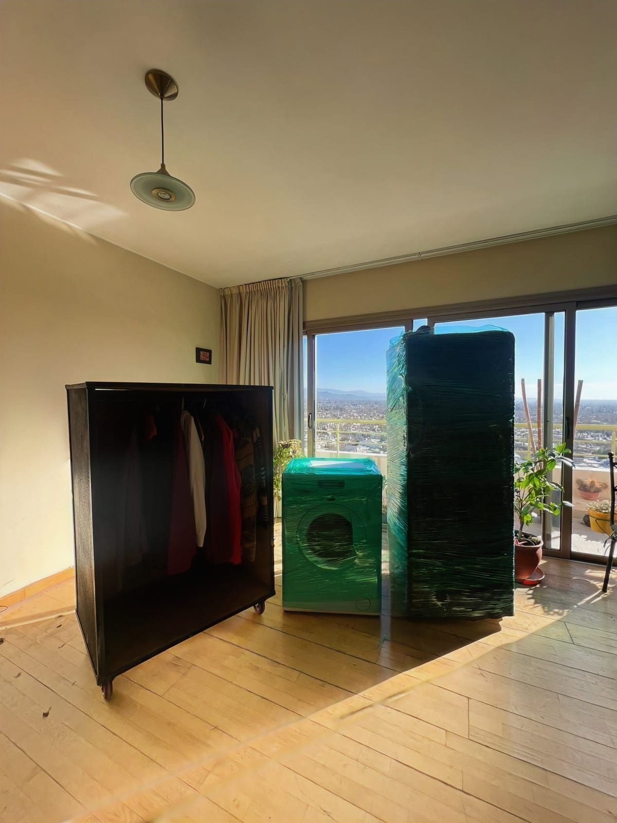Una habitación con muebles plastificados: un armario, una lavadora y un panel alto. Luz solar por la ventana.