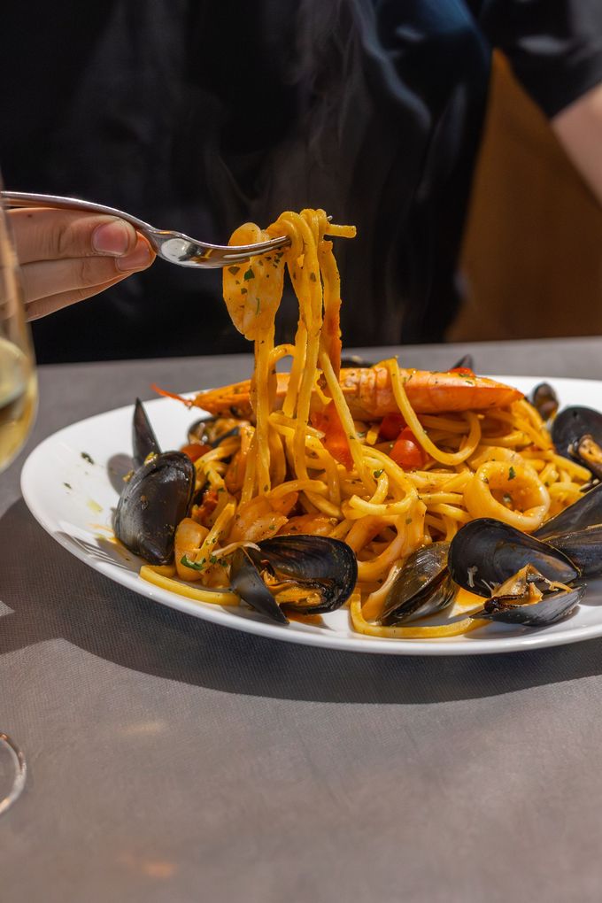 Forchetta che solleva spaghetti e cozze da un piatto bianco con salsa di pomodoro su un tavolo