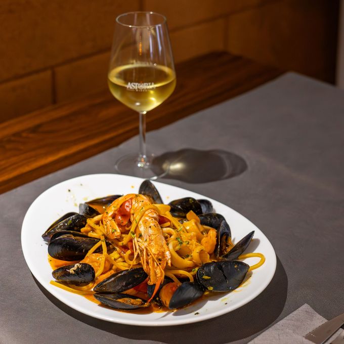 Un piatto di cozze nere e pasta con gamberi accanto a un bicchiere di vino bianco su un tavolo di ristorante.