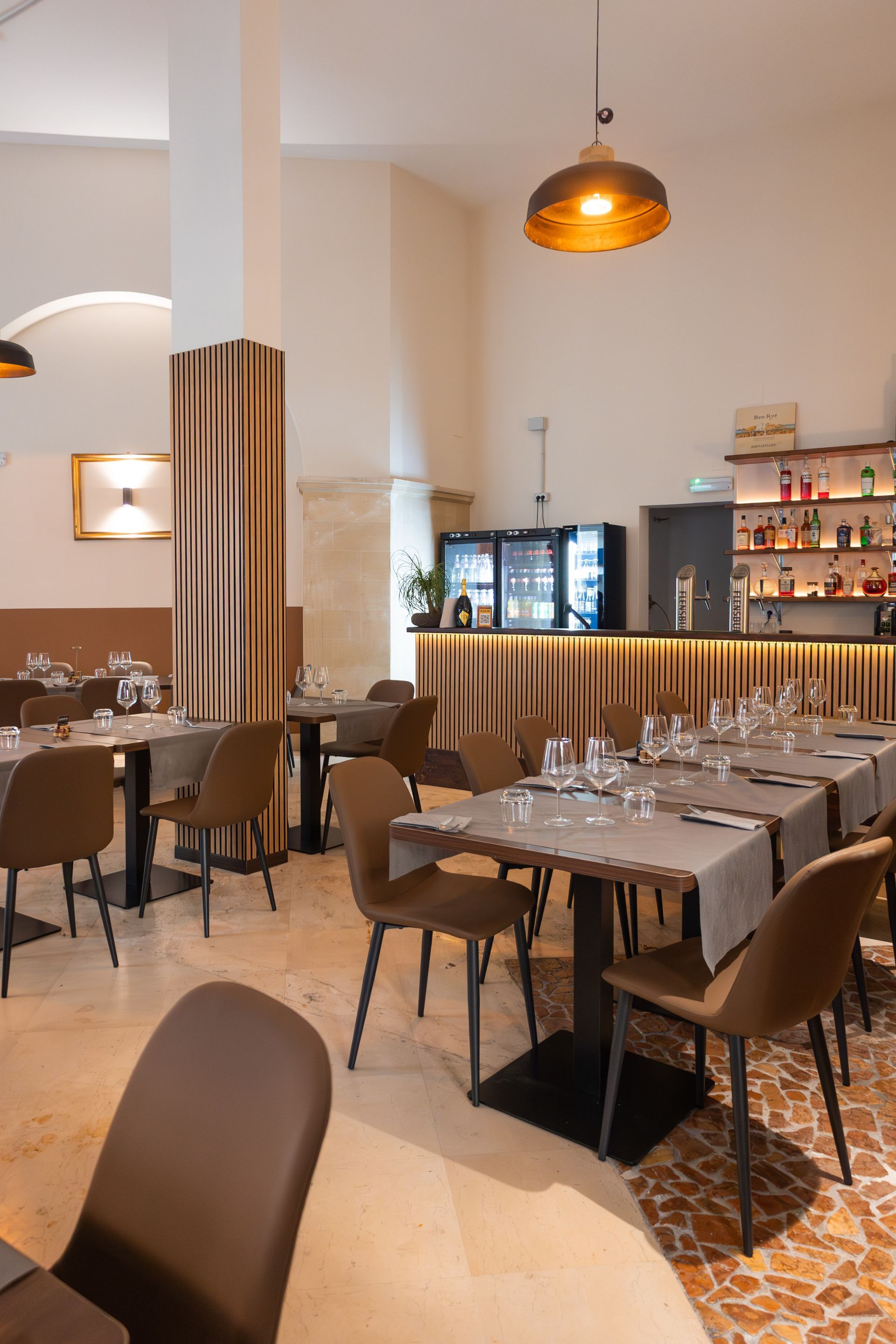 Elegante sala da pranzo di un ristorante con tavoli apparecchiati, luci soffuse e un bar sullo sfondo.