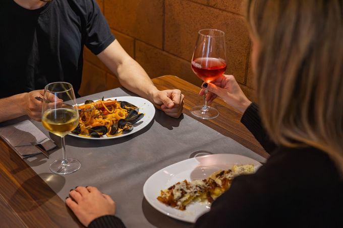 Due persone che cenano a un tavolo, con pasta, bicchieri di vino e un'atmosfera accogliente da ristorante.