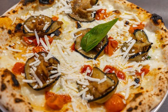 Primo piano di una pizza con funghi, pezzi di pomodoro, basilico e formaggio grattugiato su una crosta dorata.