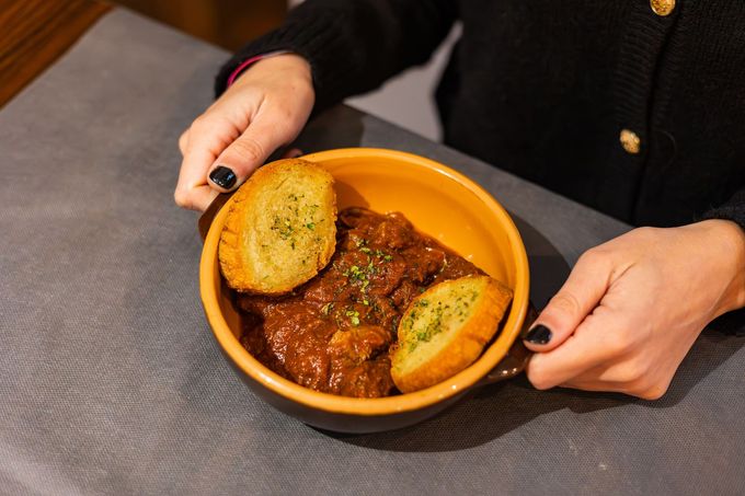 Mani che reggono una ciotola arancione di stufato con fette di pane su un tavolo