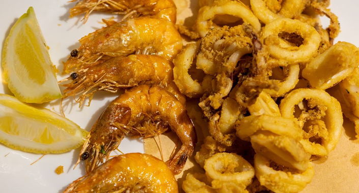 Anelli di gamberi e calamari fritti con spicchi di limone su un piatto bianco, conditi con salsa.