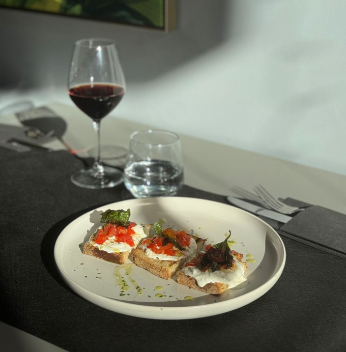 Antipasto servito su un piatto con guarnizione di pomodoro, accanto a un bicchiere di vino rosso e un bicchiere d'acqua.