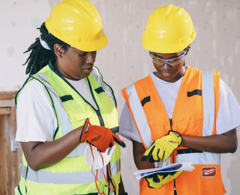Two construction workers in high-visibility vests and hard hats reviewing paperwork together on a job site.