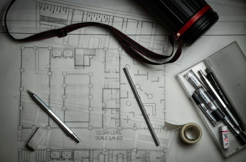 Drafting tools, a pencil, and a blueprint tube arranged on a white floor plan of a building.