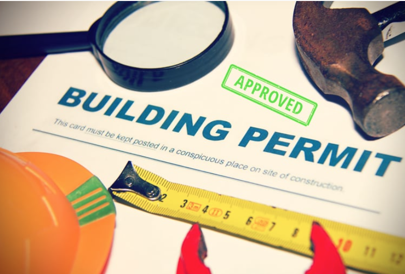 An approved building permit document surrounded by a magnifying glass, a hammer, a tape measure, and a construction hat.