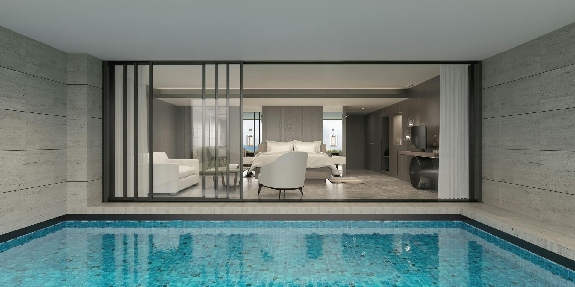 A pool with blue water sits in front of a modern, open-plan hotel suite featuring minimalist gray tones and a bed.