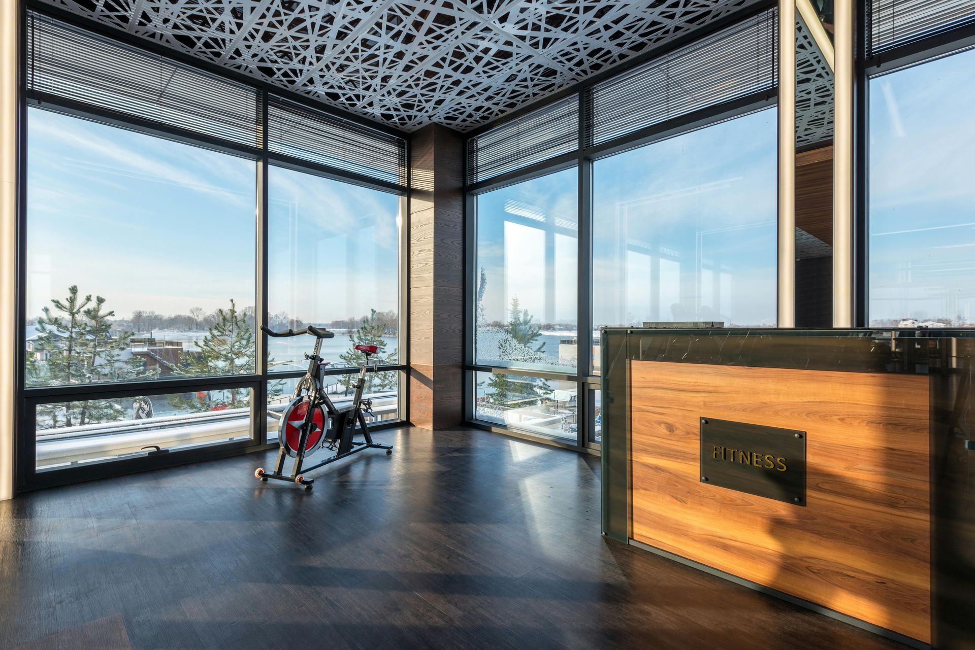 A gym space with a spin bike, wood-paneled reception desk, and floor-to-ceiling windows overlooking a snowy landscape.