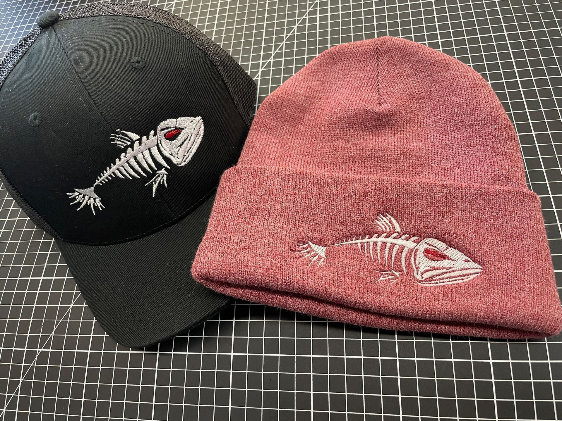 A baseball cap and a beanie with a fish skeleton on them are sitting on a table.