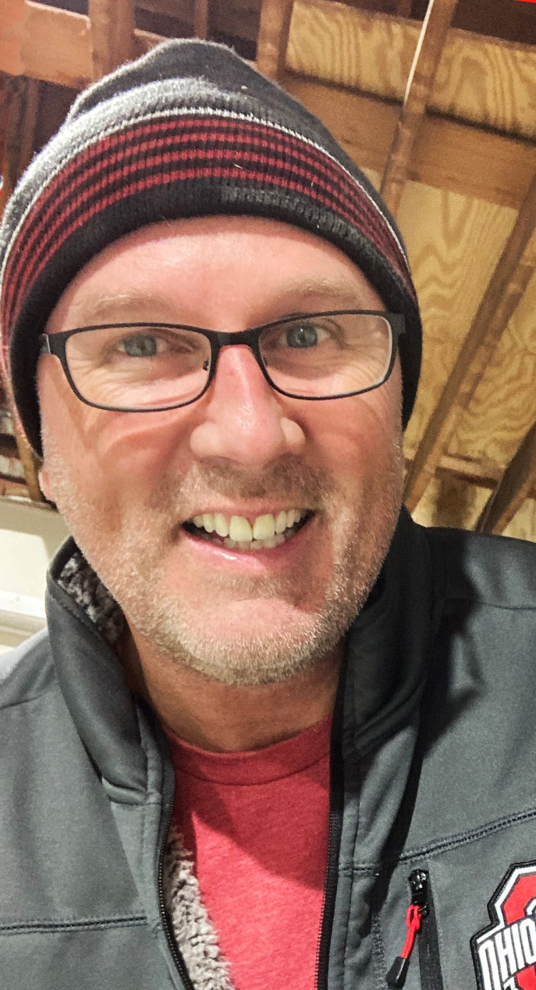 A man wearing glasses and a beanie is smiling for the camera.