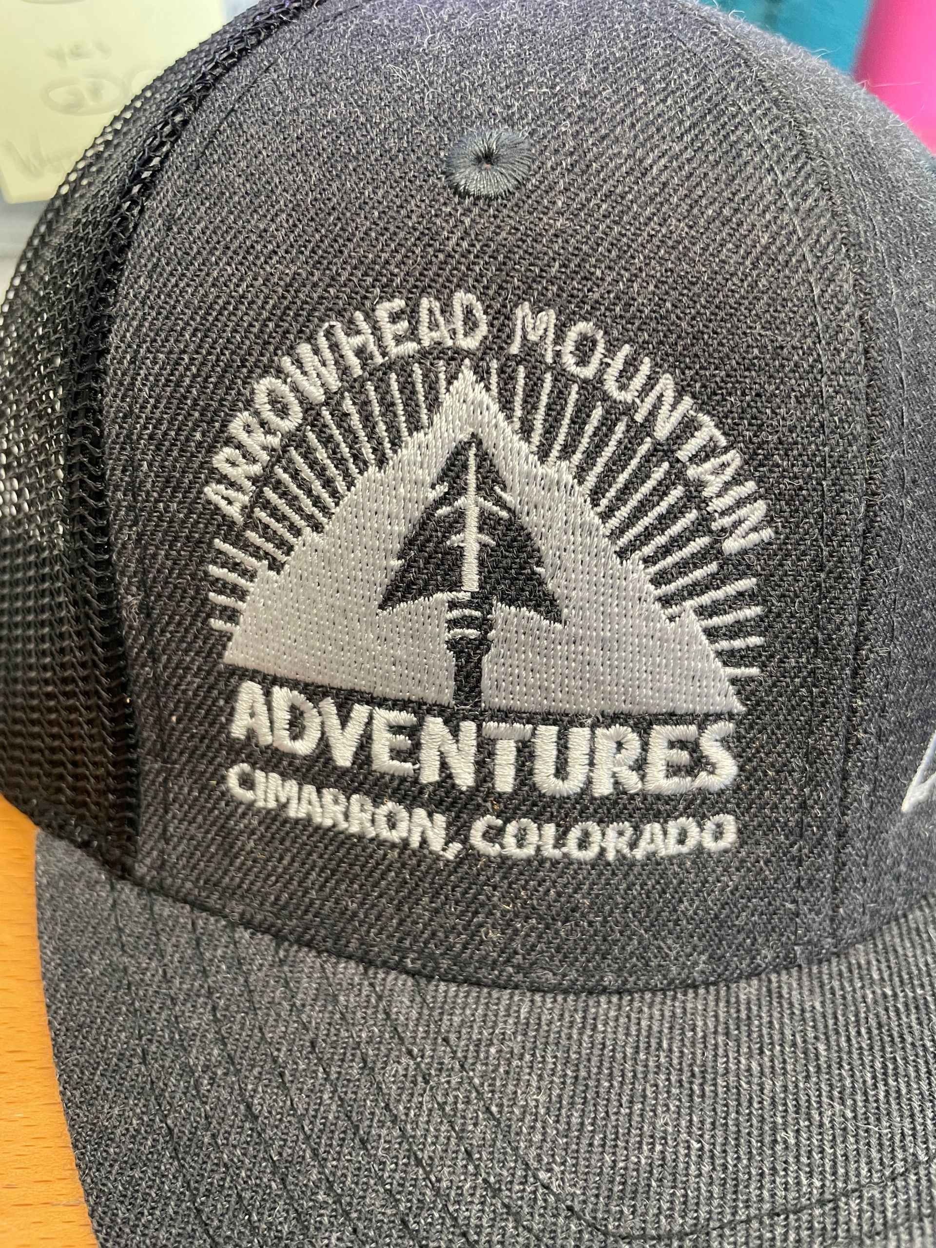 A black hat with an arrowhead mountain adventures logo on it.