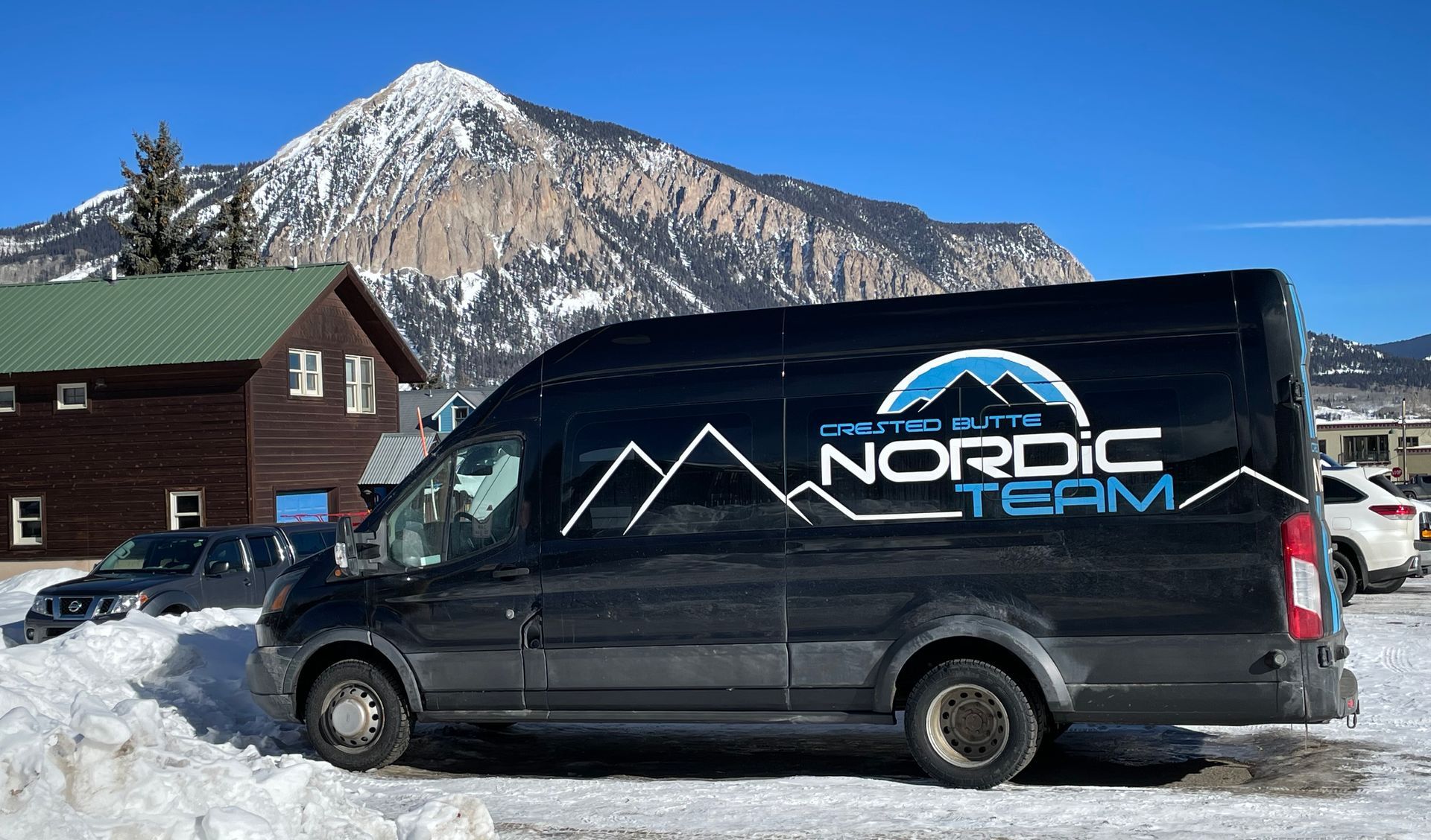 A nordic team van is parked in the snow in front of a mountain.