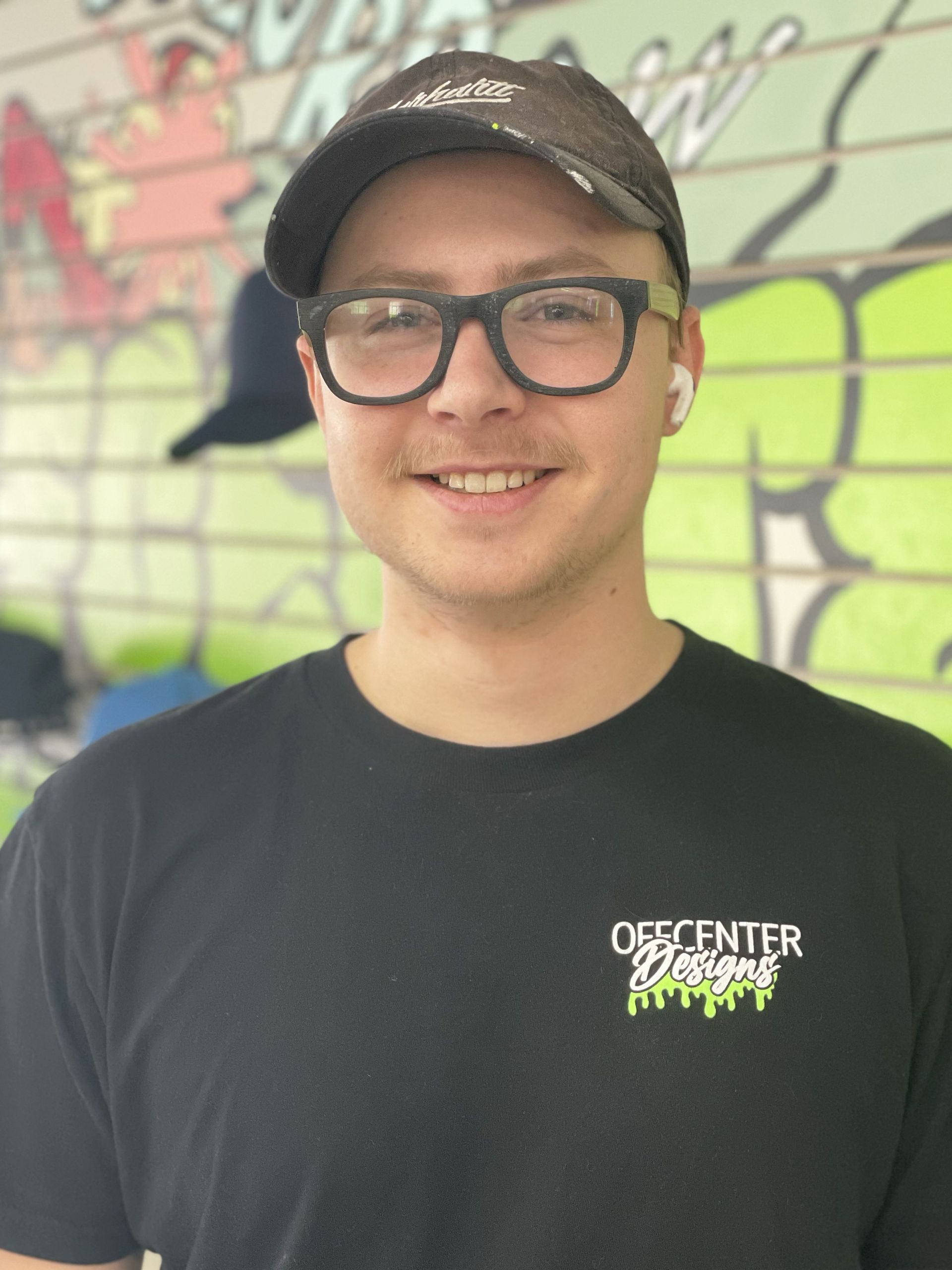 A man wearing glasses and a hat is wearing a black shirt that says descent