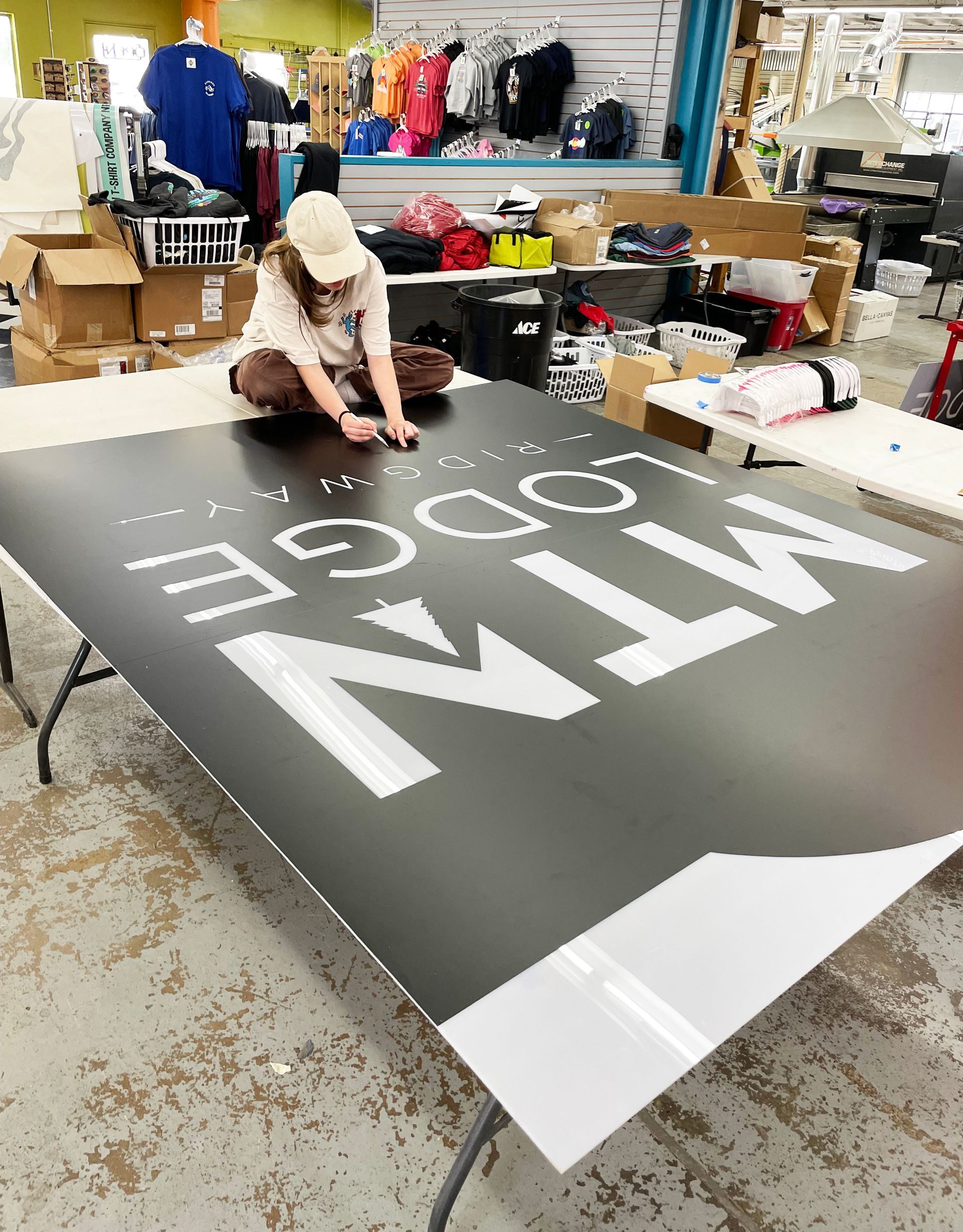 A woman is sitting on a table working on a large sign.