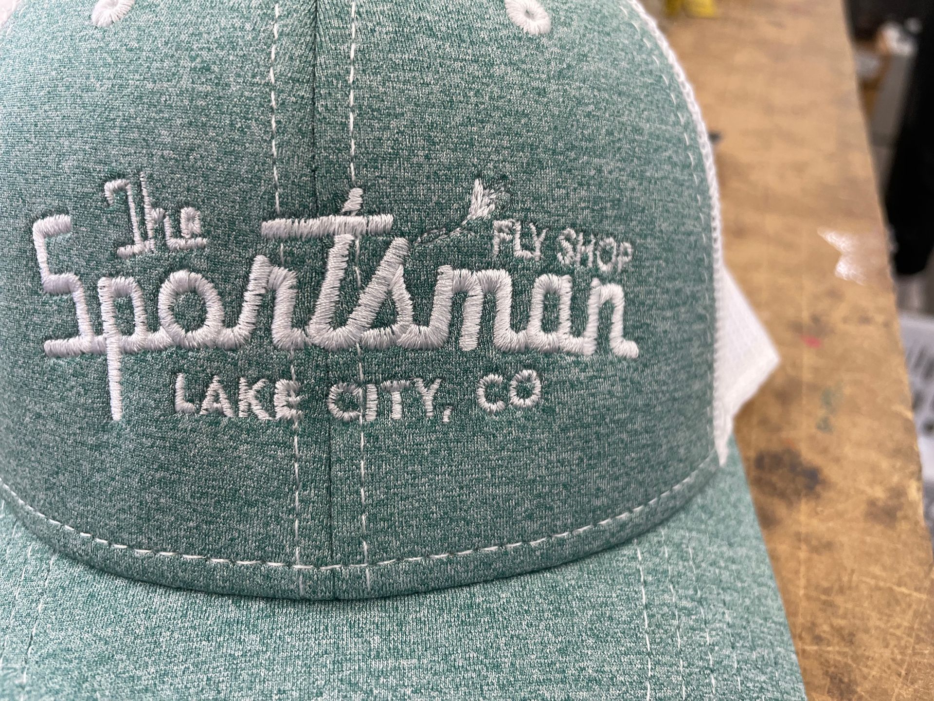 A close up of a baseball cap with the words `` the sportsman fly shop lake city co '' embroidered on it.