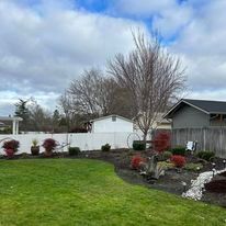 A lush green backyard with a white fence and a house in the background.